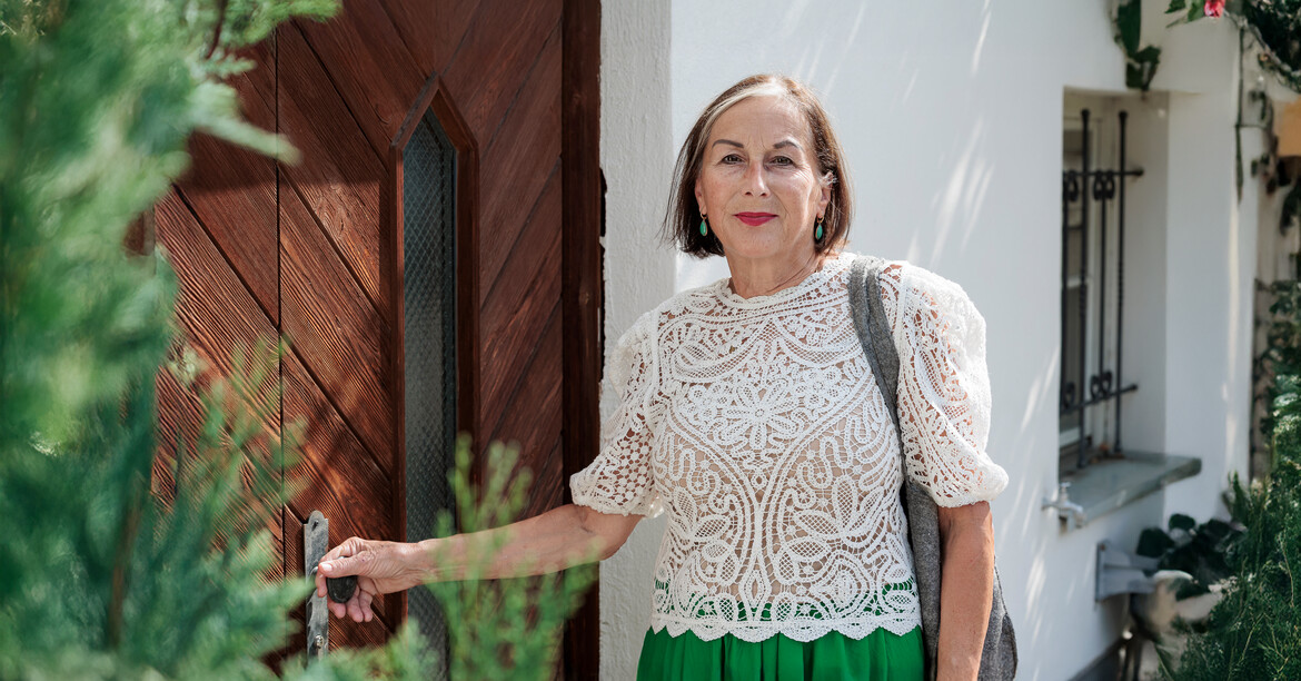 Portrait einer Haussammlerin, die an einer Eingangstüre eines traditionellen Wohnhauses in Tirol steht.