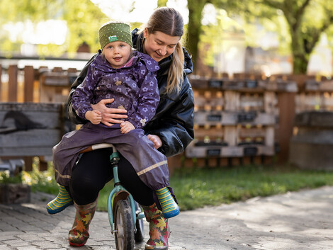 Eine Kindergartenpädagogin fährt mit einem Kinder Fahrrad.