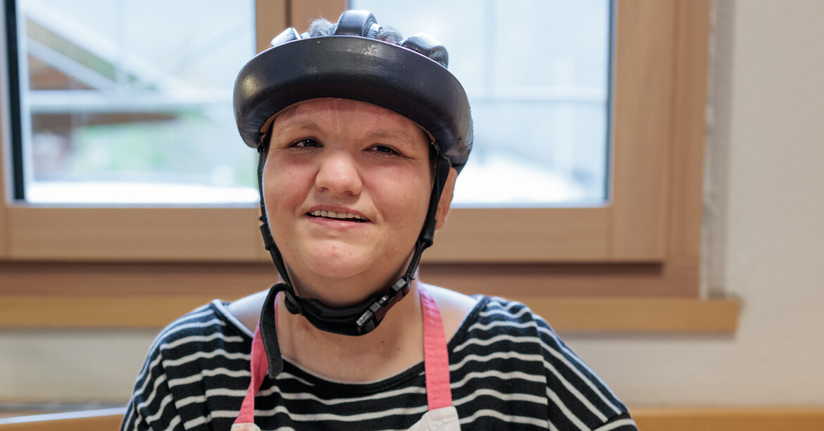 Portrait einer lachenden Frau mit Behinderung, die an einem Küchentisch Tomaten schneidet.