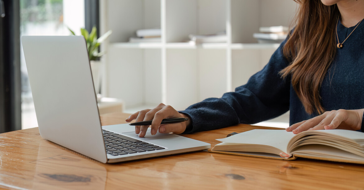 Finanzbericht 2022 gemäß den Richtlinien des Spendegütesiegels, in Euro. © Natee Meepian/AdobeStock Eine Frau sitzt an einem Holztisch und hat ein Buch vor sich aufgeschlagen sowie einen Laptop aufgeklappt.