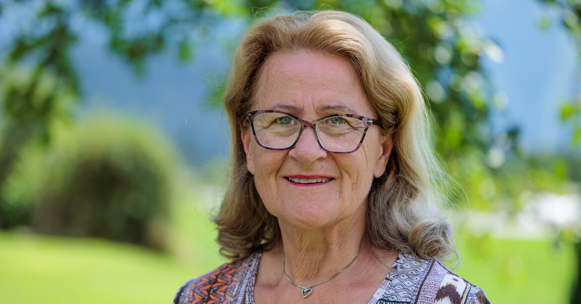 Portrait einer Seniorin mit Brille, die im Sommer in einem grünen Garten steht.
