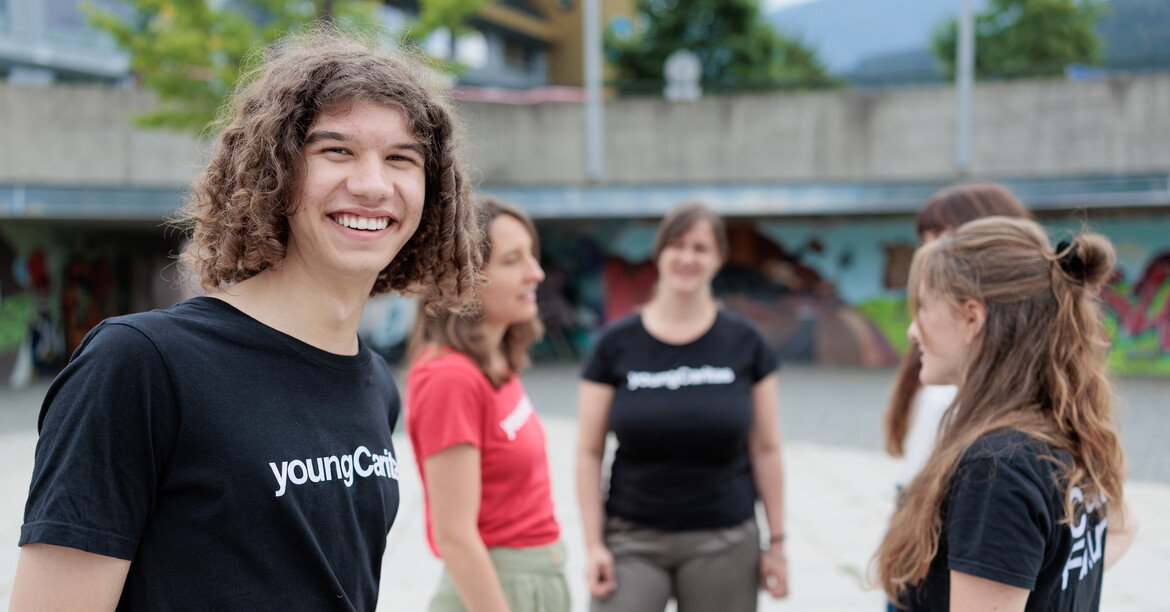 Portrait eines Freiwilligen mit schwarzem youngCaritas T-Shirt, der mit vier Kolleginnen auf einem großen Platz steht.