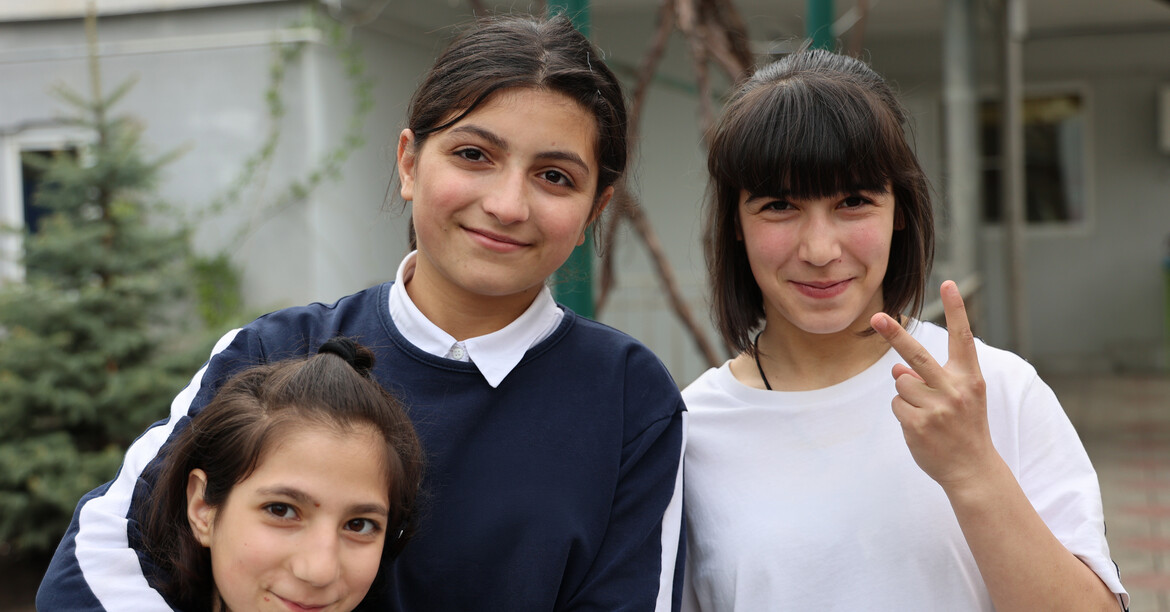 Drei lächelnde Schüler*innen stehen zu einem Gruppenfoto zusammen.